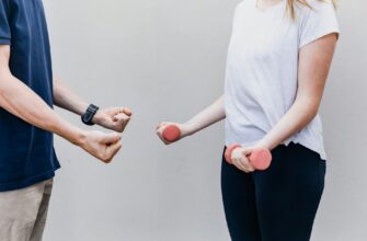 Мужчина показывает девушке упражнение с гантелями